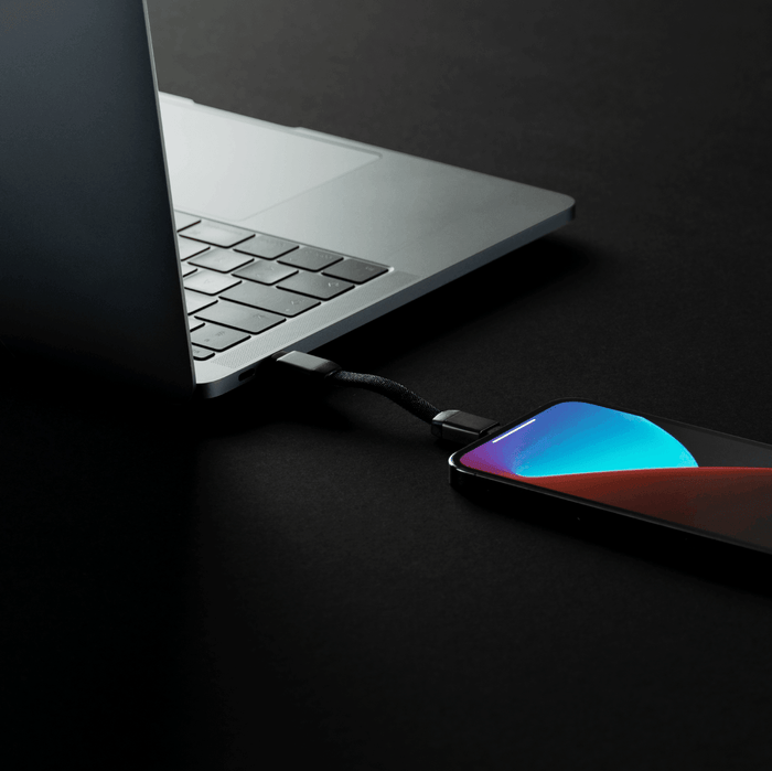inCharge® Mini - The Smallest cable ever - inCharge® Mini - The Smallest cable ever - USB to Lightning - Compact black charging cable connected between a sleek silver laptop and a smartphone with a vibrant blue and red gradient. - Rolling Square inCharge® Mini - The Smallest cable ever - USB to Lightning - Compact black charging cable connected between a sleek silver laptop and a smartphone with a vibrant blue and red gradient. - Rolling Square