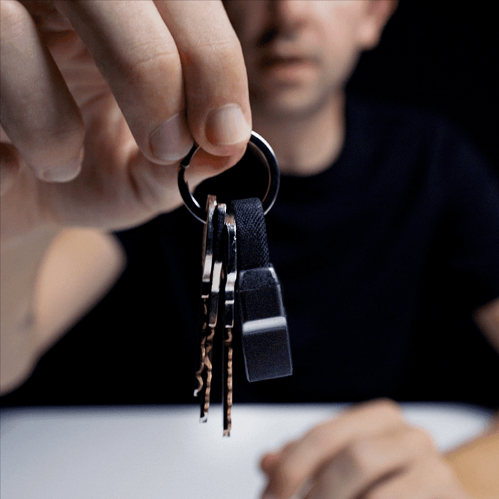 inCharge® Mini - The Smallest cable ever - inCharge® Mini - The Smallest cable ever - USB to Lightning - Compact black charging cable attached to keyring held by a hand against a dark background. - Rolling Square inCharge® Mini - The Smallest cable ever - USB to Lightning - Compact black charging cable attached to keyring held by a hand against a dark background. - Rolling Square