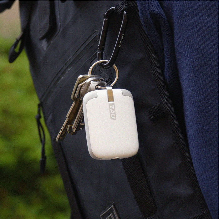 TAU® - Always-charged power bank - TAU® - Always-charged power bank - Charcoal Black - Compact white power bank with rounded edges attached to black backpack by carabiner clip alongside several keys. - Rolling Square TAU® - Always-charged power bank - Charcoal Black - Compact white power bank with rounded edges attached to black backpack by carabiner clip alongside several keys. - Rolling Square