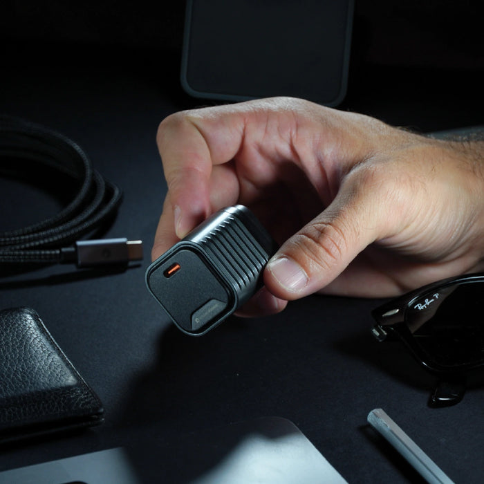 Supertiny 65W - US - Compact black 65W charger with USB-C port clearly shown held in hand over dark surface with cables and accessories. - Rolling Square